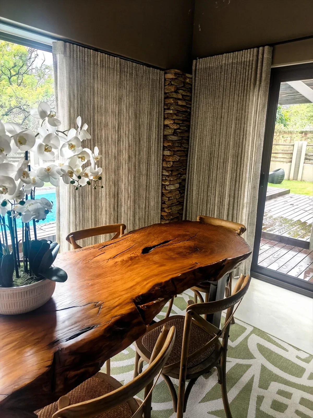 Textured wave sheers framing a dining space with a live-edge table and views to the pool and garden